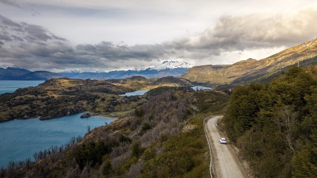 A drone view of a car on the Carretera Austral highway in Aysen. Chile, with mountains and lakes.